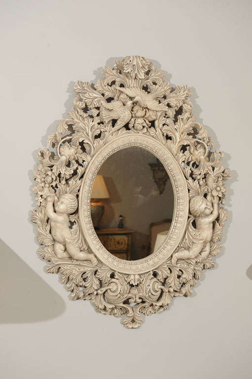 An elaborately carved oval mirror with putti and follage with birds.
