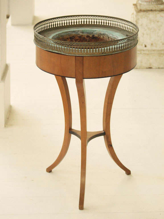 A veneered plant stand with three sinuous, curved legs joined by a stretcher, the walnut veneer accented with an ebonized inlay trim.  The stand supports a deep metal, two handled liner with a tall, pierced gallery.
