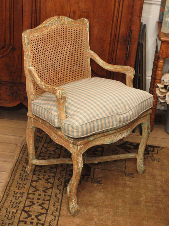 Beautiful Regence Fauteuil in light walnut. Detailed carvings on the frame have touches of light green. Cane back and seat are in perfect condition. New down cushion with French blue linen check. This is an elegant Regence chair in excellent