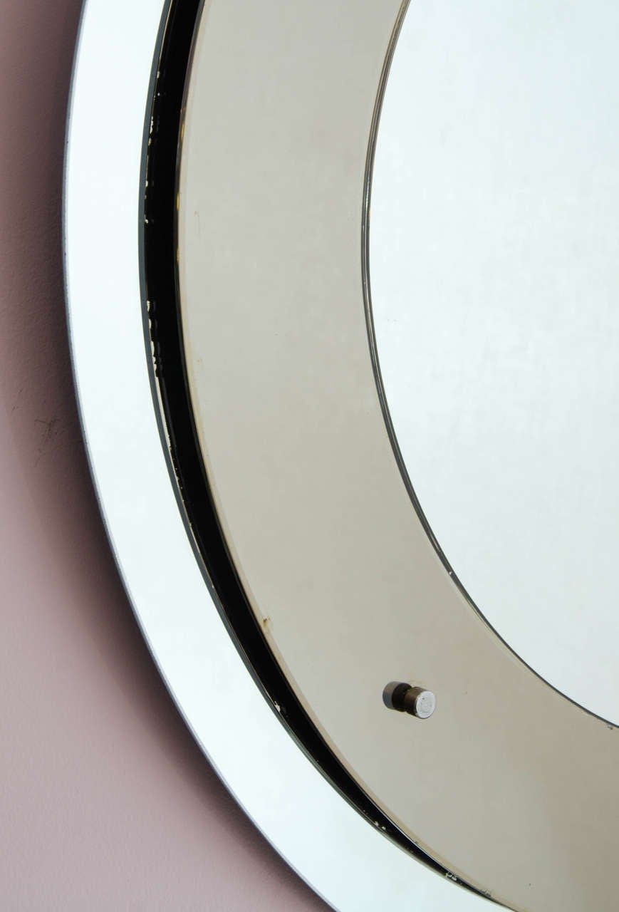 1960s wall mirror attributed to Max Ingrand for Fontana Arte, with bronze-tinted mirrored disc in front of circular silver mirrored back plate attached by four circular chrome rivets.