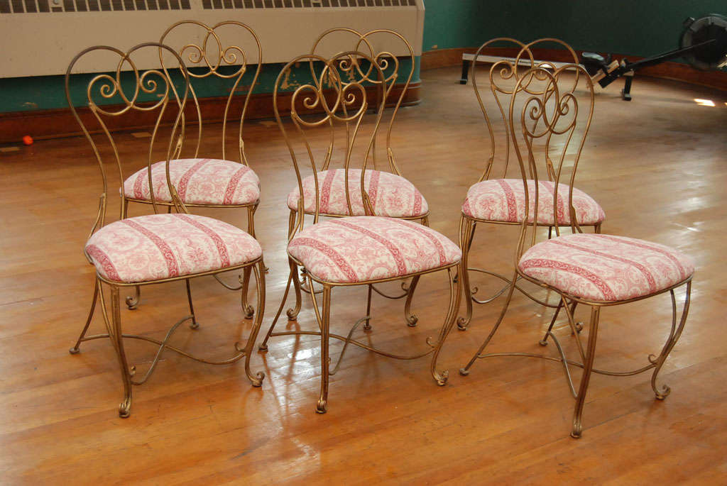 This set of six chairs made of heavy wrought iron are hand forged. With tall scrolling backs and deep wide seats they are comfortable and well proportioned. The set is painted in an old gold paint with many rub thrus and with a great surface from