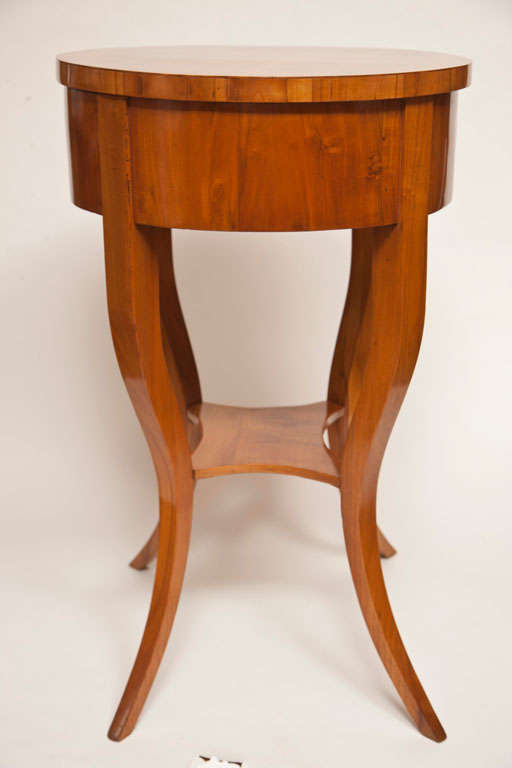 early Biedermeier blonde cherry wood circular side table with sliding top opens to reveal an original pin cushion and useful storage, finishing on four sinuous legs