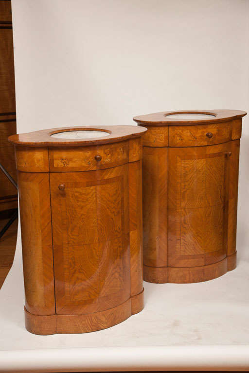 Unique pair of French Art Nouveau oval shaped cabinets with inset carrera marble tops on elmwood veneered bases, finished on all sides and comprised of a drawer and door. useful as tall side tables, nightstands, corner pieces or as pedestal stands.