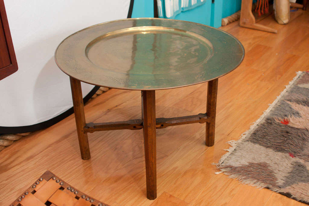 Brilliant wood-hinged folding table with octagonal legs and chamfered stretchers. Table receives circular brass tray with hand-incised floral border.