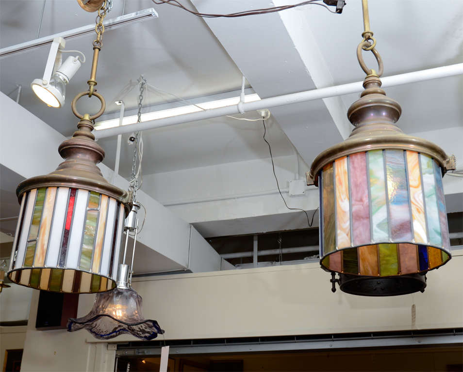 A pair of Arts and Crafts pendant lights. Each one is composed of original stained glass panels in various colors and bronze fittings. They have been recently rewired.