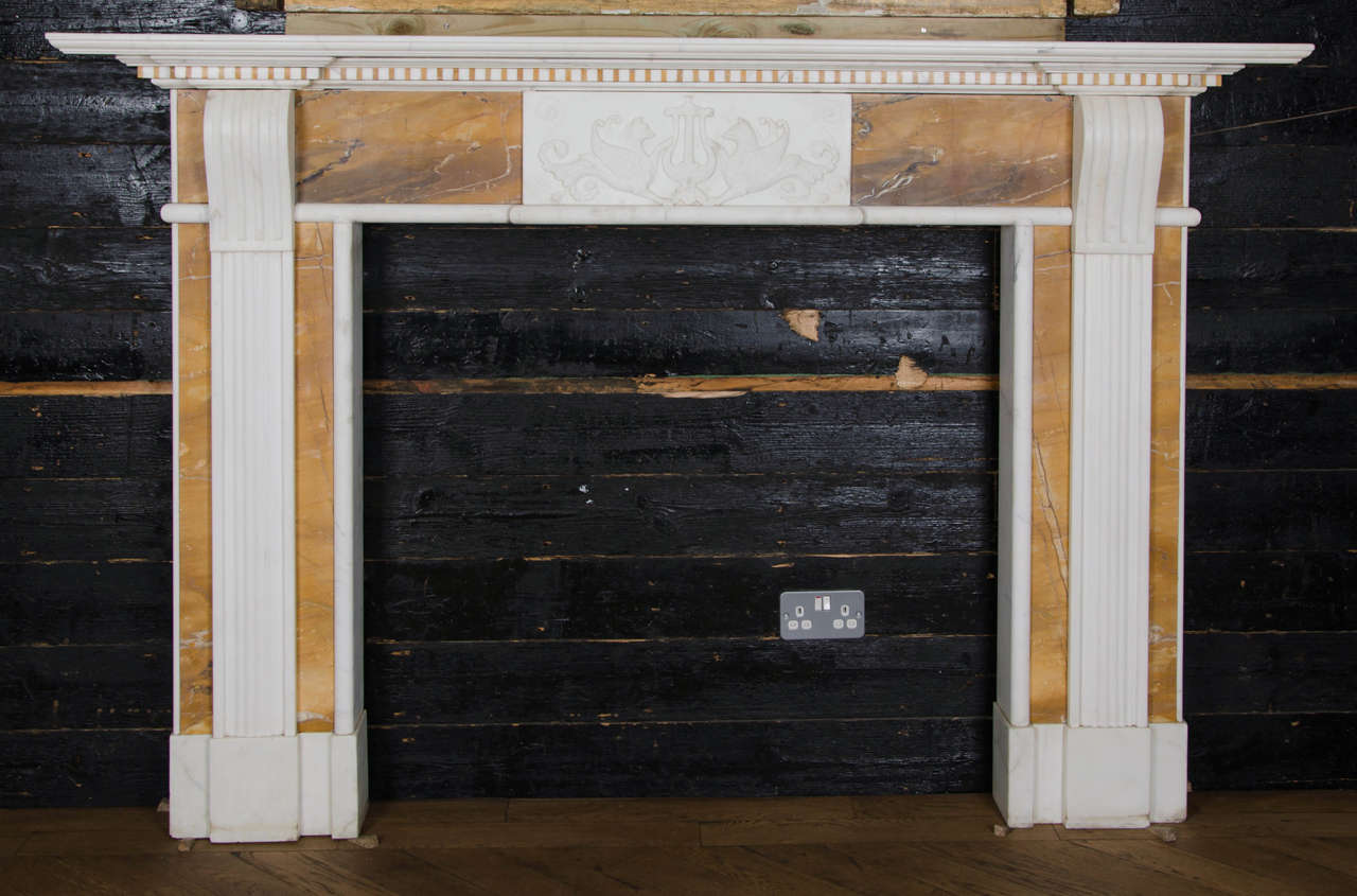 A striking, stately fireplace surround in off-white statuary marble with characterful sienna marble inlay. This Georgian style fire surround has wide, imposing proportions with a moulded shelf and fluted columns in the jambs. The columns are