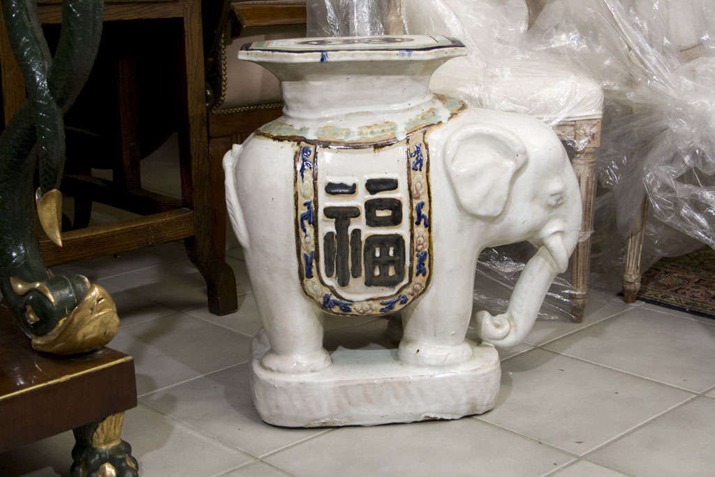 Elephant- form white glazed with a saddle blanket decorated with symbols and a decorated seat on top. Cobalt and turquoise glazed details.