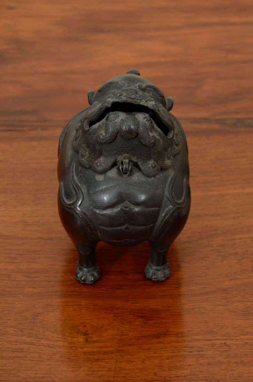 This Chinese small bronze censer, or incense burner, dating from the late Ming or early Qing dyansties, was cast as the figure of a Buddhistic lion standing on four feet, the head, with open mouth, single horn and curled mane, hinges open to the