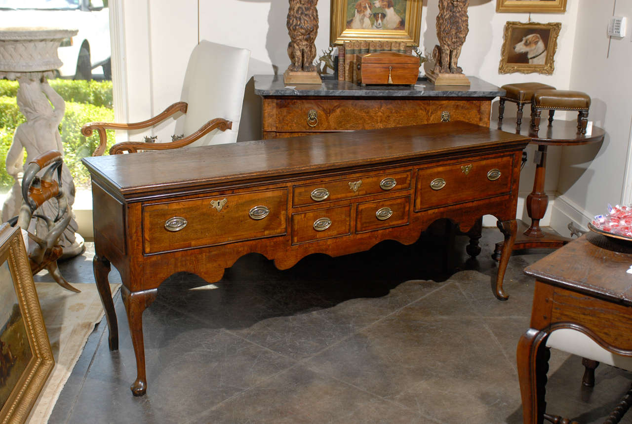 An English Georgian wooden sideboard from the early 19th century with five-drawers, cabriole legs and scalloped apron. This English sideboard (actually dresser base) circa 1820 features a rectangular top over a large apron decorated with