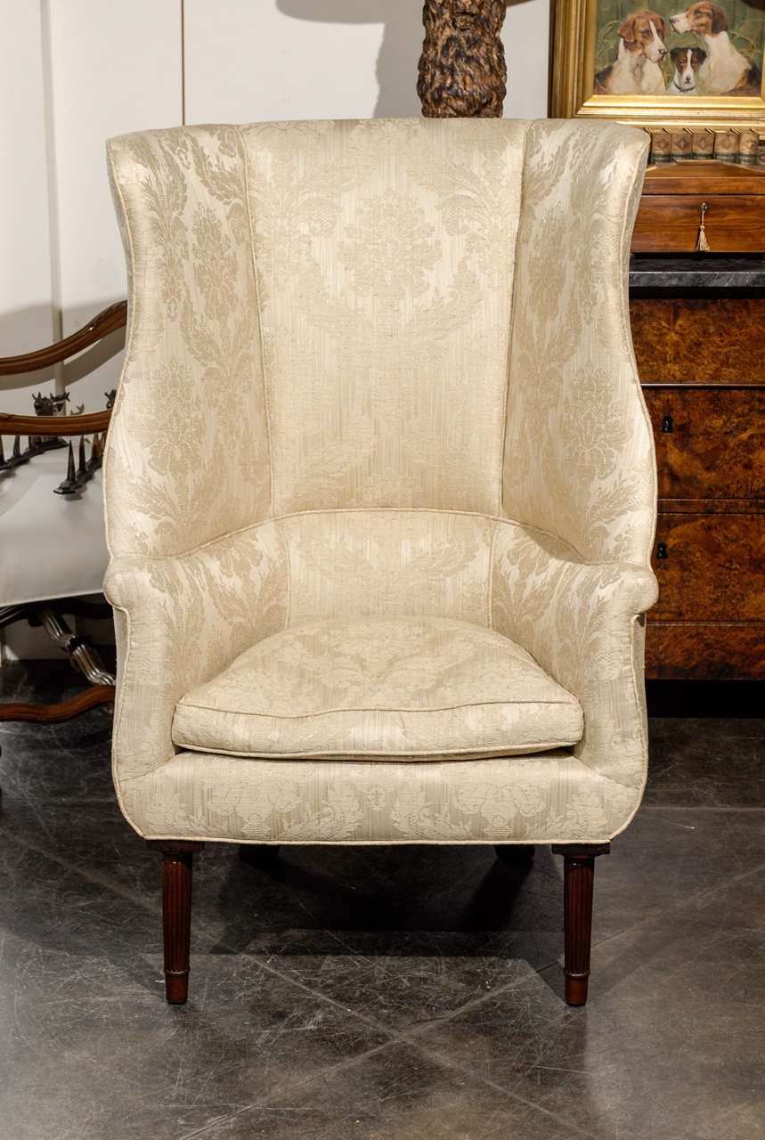 A large upholstered barrel back wing chair on reeded legs from the early 20th century. This impressive wing armchair is dated circa 1920 and is raised on four round reeded and tapering legs. This wing chair features a large barrel back, a distant