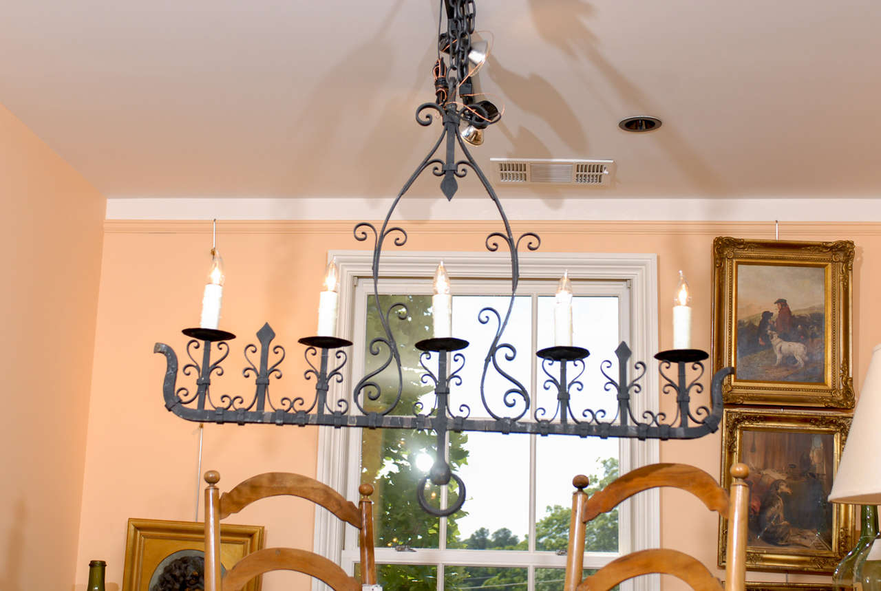 A French wrought iron five-light chandelier from the mid-20th century with authentic wax sleeves. This French iron chandelier circa 1940 features a single row of five electric lights, adorned with a symmetrical scrolled décor. The 1940s, showed the