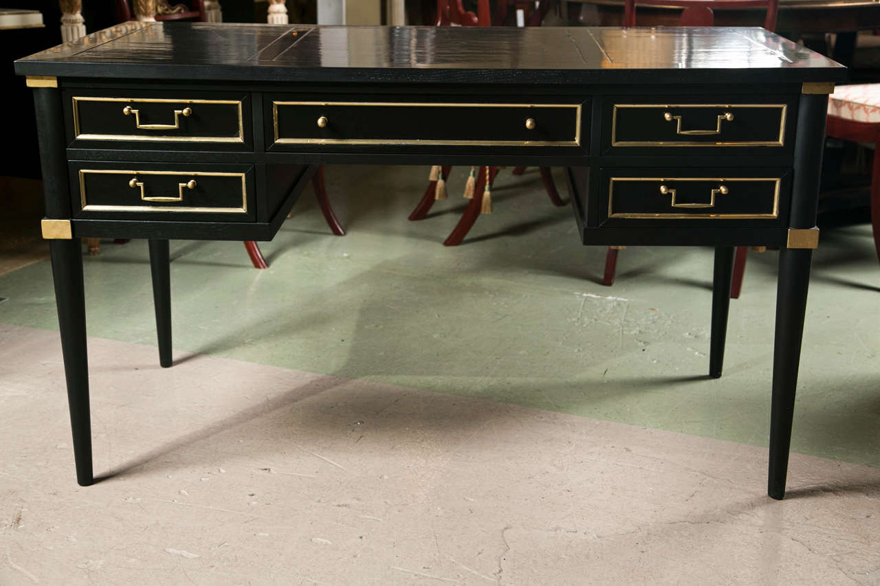 French Directoire style bureau plat, overall ebonized with parcel-gilt banding, the rectangular writing surface atop a long narrow drawer flanked by two smaller drawers on each side, raised on tapering circular legs. By Jansen.