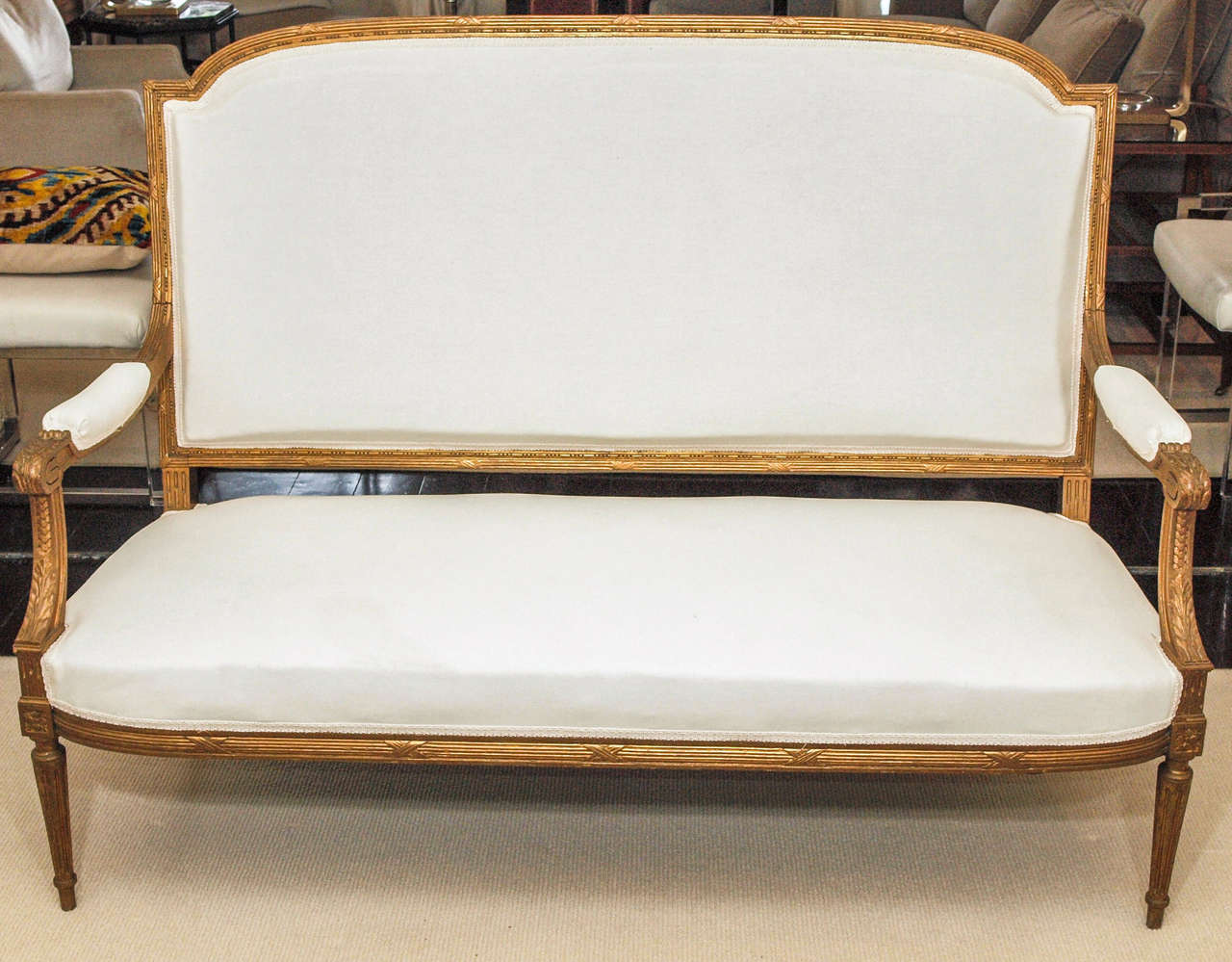 Lovely high-back settee in the Louis XVI taste; gilt beechwood with padded arms, out-curving seat and attenuated tapering reeded legs; subtly carved throughout with losses to the gilt appropriate to age and use; now upholstered in white muslin