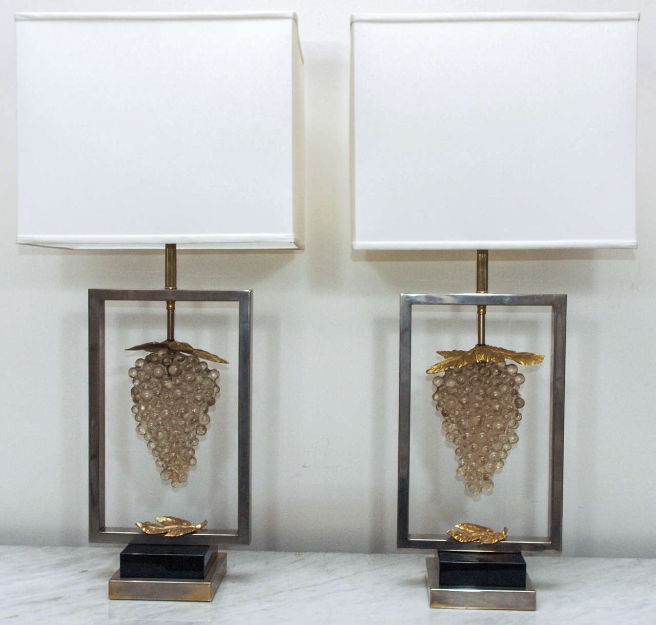 Pair single light table lamps attributed to Maison Jansen, each with a cluster of pressed glass grapes as the focal point; structure in chrome-plated brass with plinth in black lacquer; the grape leaves in gilt metal; shades in white linen; in-line