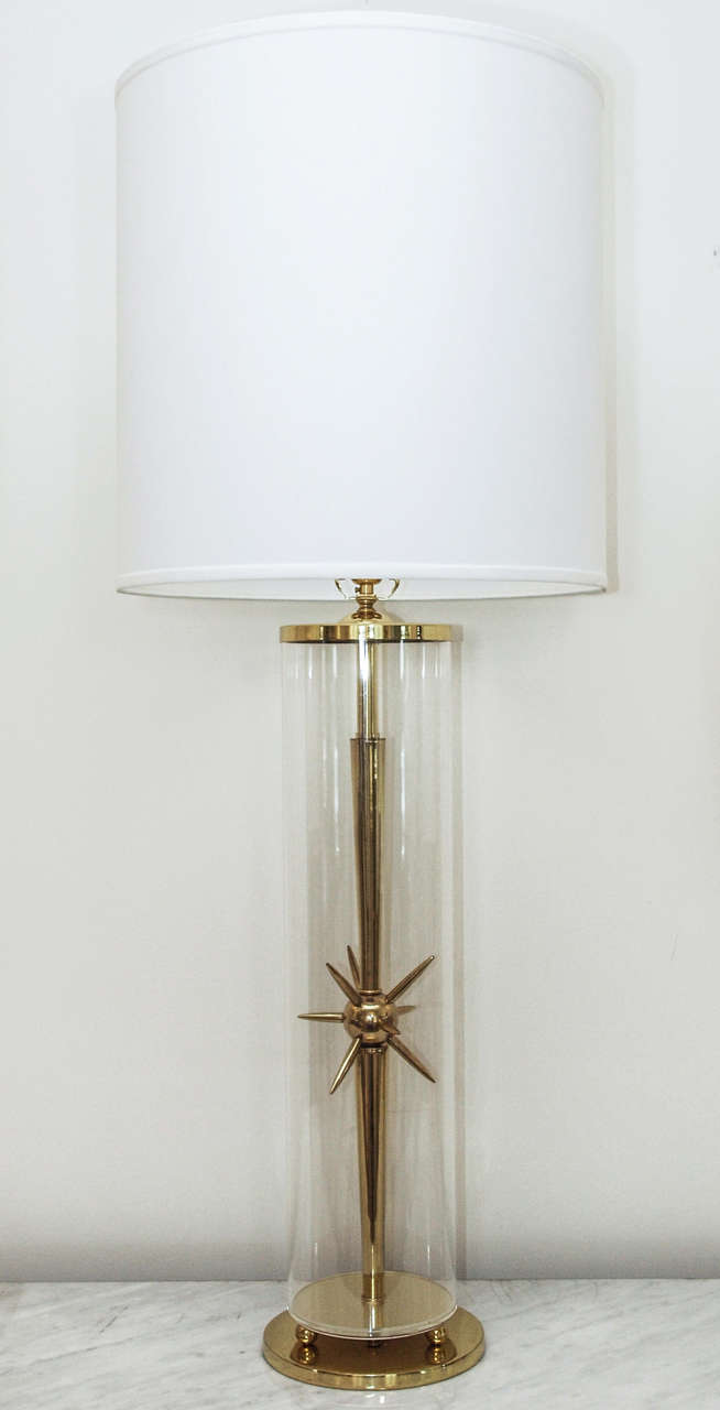 Table lamp in brass and acrylic; the central brass stem with "sputnik" motif inside a clear acrylic cylinder raised on ball feet above the 7.5" diameter circular base; shade in hard-backed ivory silk; measurements include the shade