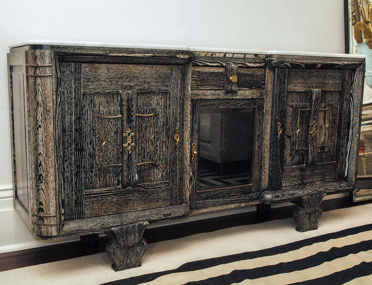 Handsome credenza in black oak ceruse with conforming white marble plateau; the center opening with glass door below a single drawer; the outer openings with solid doors concealing adjustable shelves; shaped and carved front legs; bronze scrolling