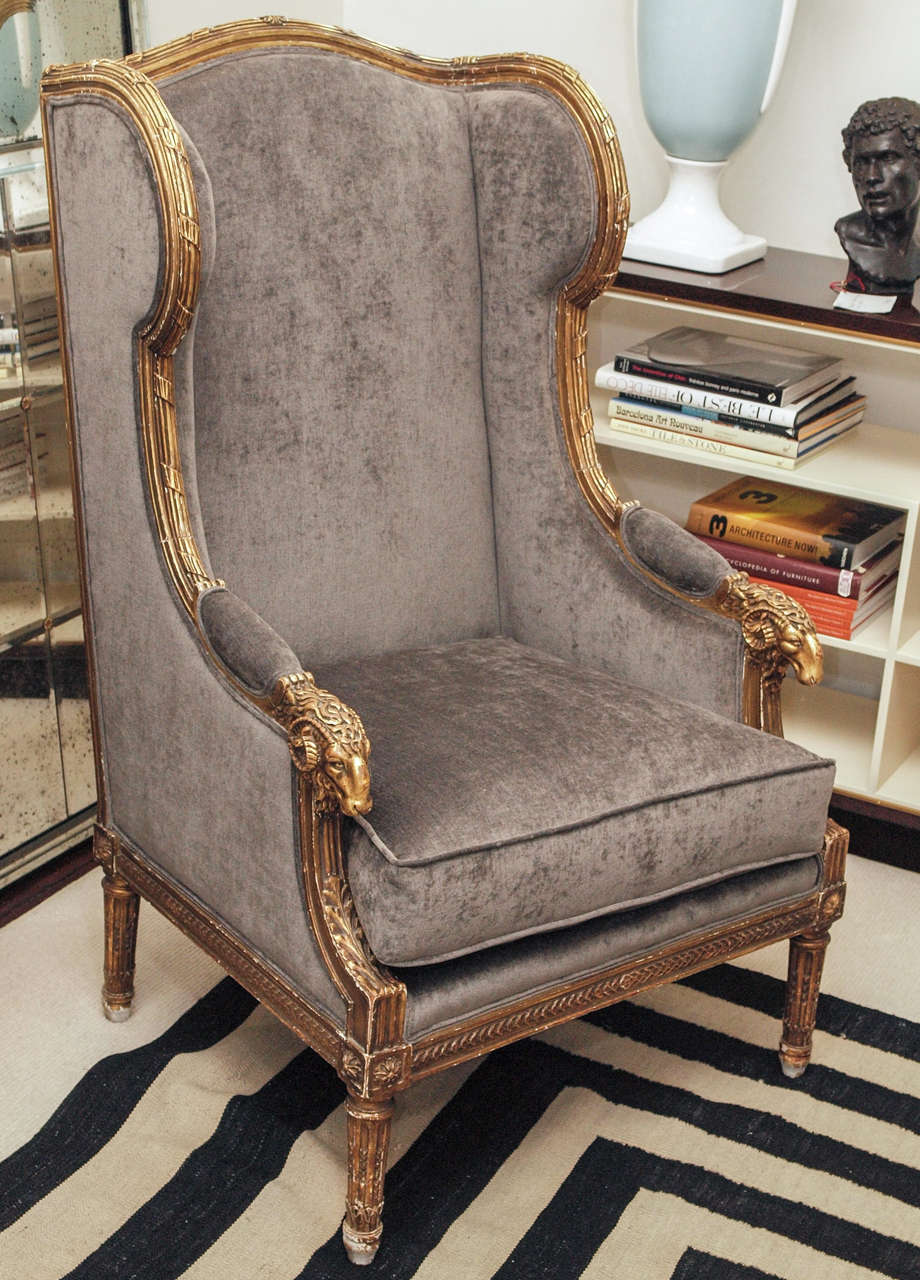 Highly carved and heavily gilded wing-back armchair in the Louis XVI taste; loose seat cushion; padded armrests; now upholstered in gray silk velvet