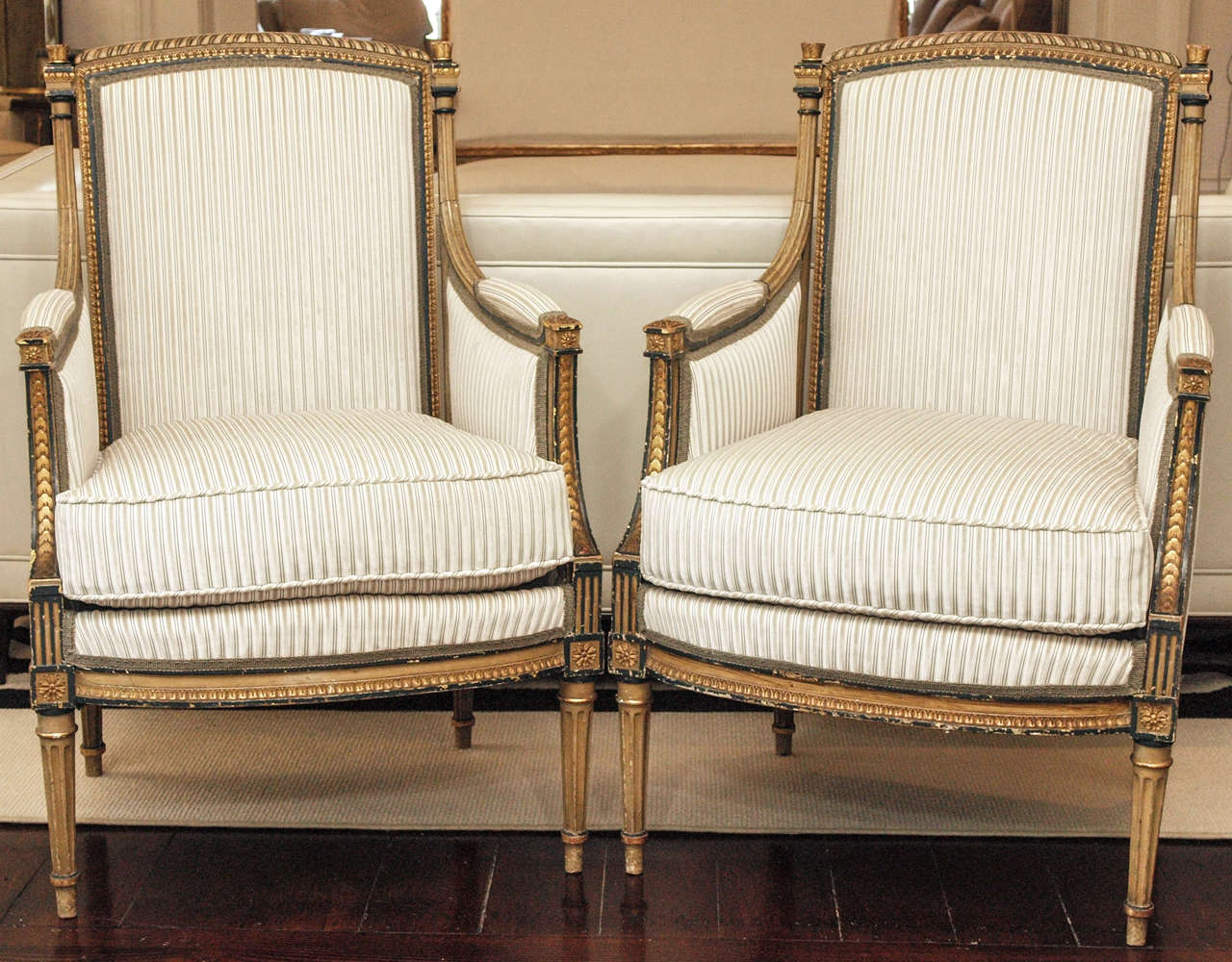 Two bergeres with ebonized and gilt frames, attractively carved and detailed; now upholstered in cream and taupe Manuel Canovas stripe; loose seat cushion