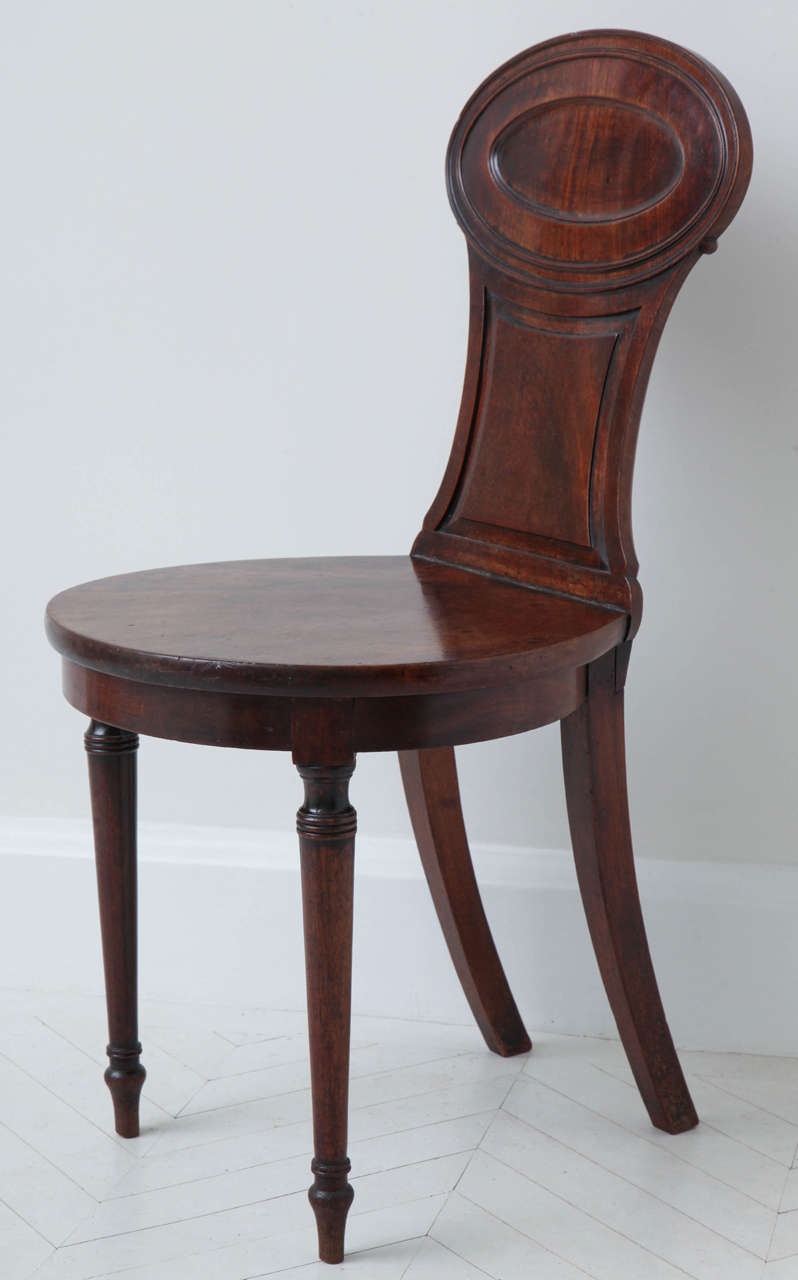 An early 19th century English Regency carved mahogany hall chair
with panelled oval back and ovoid seat, circa 1810