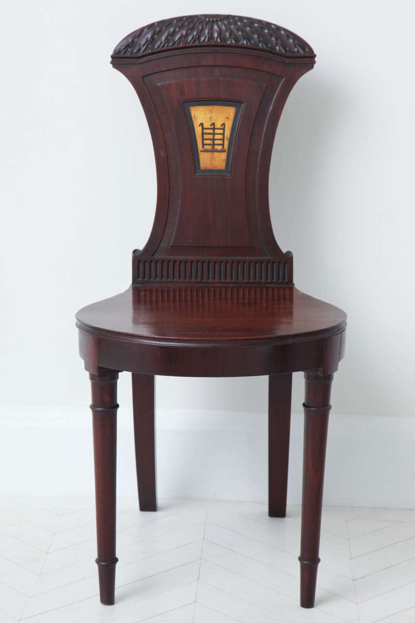 A fine pair of English Regency mahogany hall chairs with carved sunflower crest rails, fluted backs and polychrome painted portcullis crests, circa 1810.