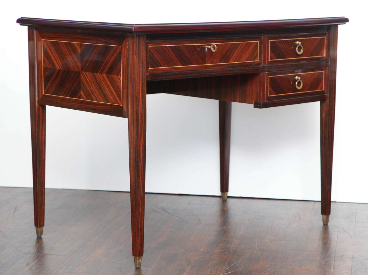Elegant desk of rosewood veneers, with book matched details and light wood inlays.  Classic and modern form with brass pulls and sabots.  Finished on all sides.