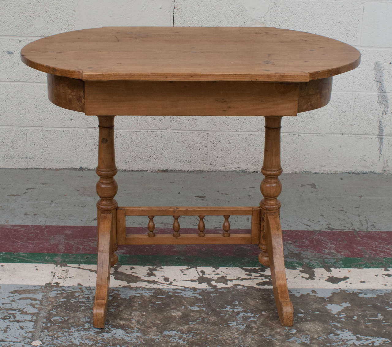 An unusually decorative pine side or center table. The stylized oval top is supported by two trestles, each with a central turned post and two gracefully curved feet, joined by a gallery of turned spindles.