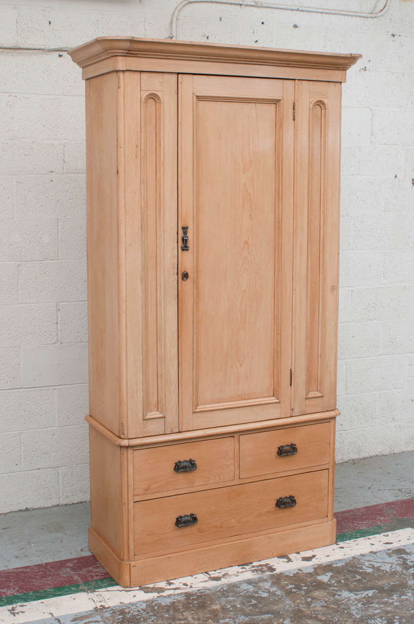 An outstanding single door pine armoire with an architecturally paneled front, gently rounded corners and a bold crown. The wardrobe section is mounted on a base of three deep delicately hand-cut dovetailed drawers.
The pine used in this piece is
