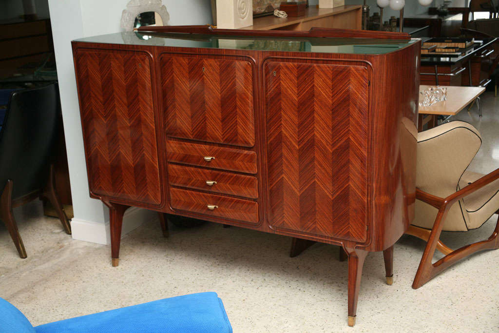 the inset green glass top above a drop down bar cabinet flanked by cabinet doors and a set of 3 drawers below the bar, all with finely executed herringbone patterns veneers