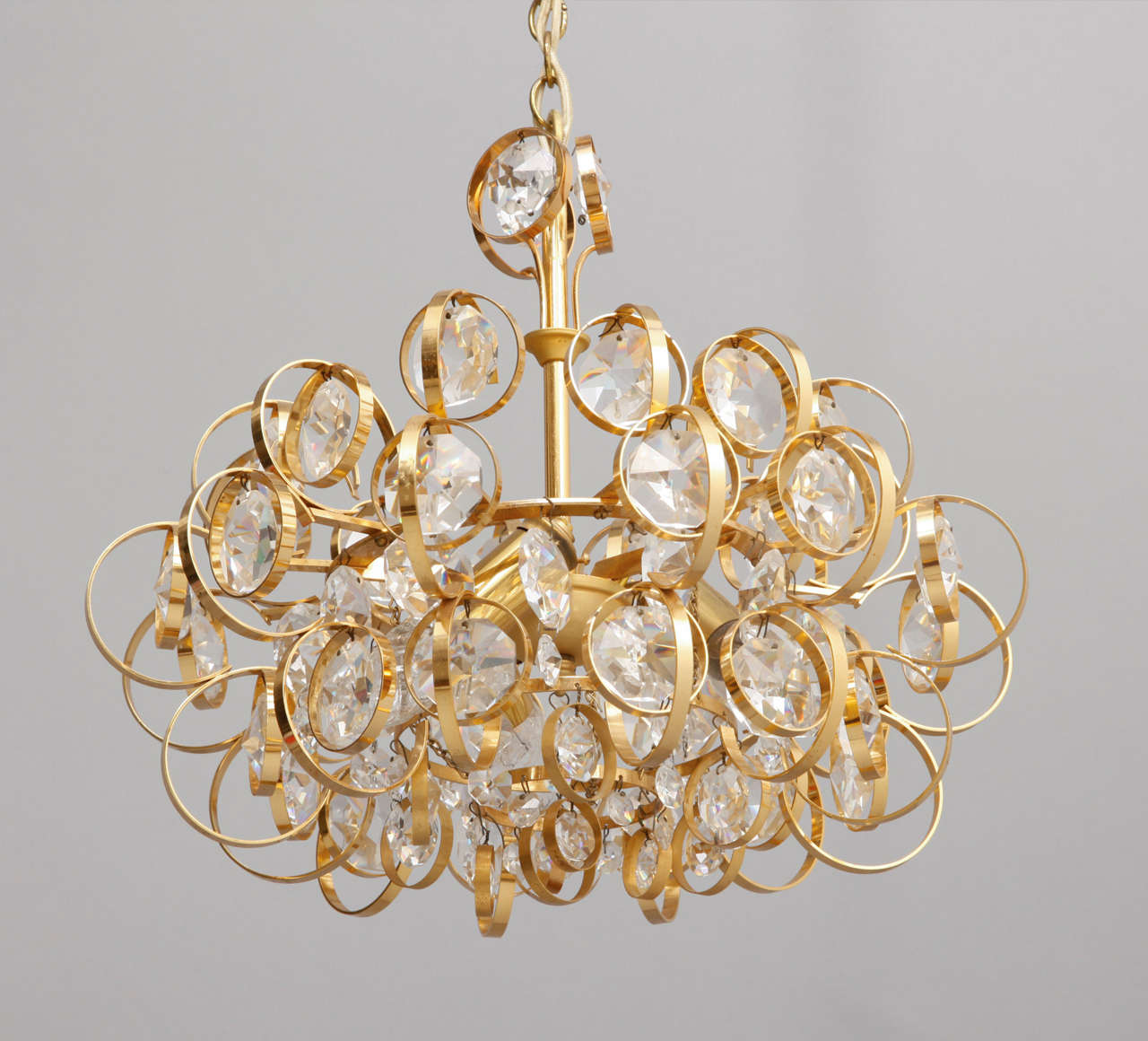 Elegant round chandelier made of textured gilt brass with crystal prisms within the outer rings of the chandelier structure as a jewel-like lamp, brilliant with lights.