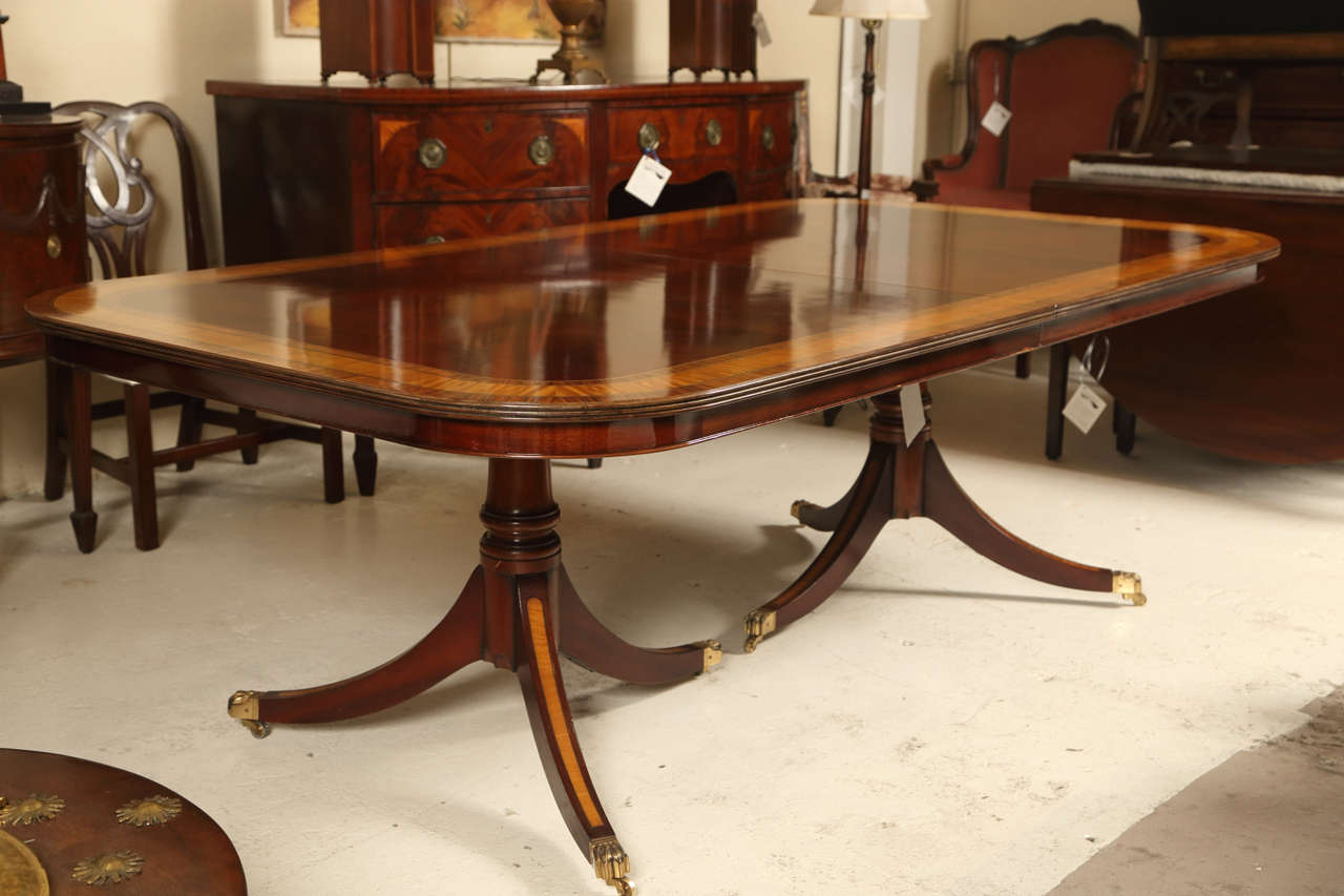 A custom quality double pedestal satinwood banded dining table. The whole resting on bronze claw feet with casters leading to sprayed triple column support legs with mahogany and satinwood banding. The top having recently been refinished to its