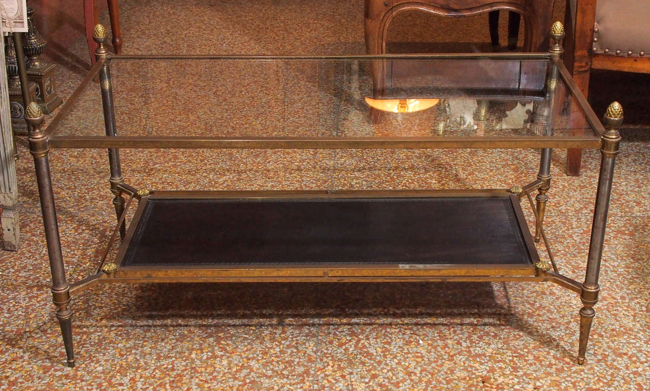 A mid-20th century glass, brass and leather two tier coffee table.  Black leather embossed with greek key motif and glass top corners capped with acorn finials.