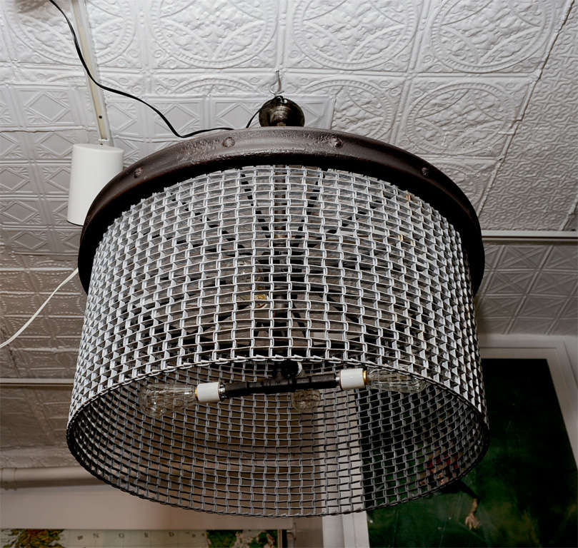 Factory conveyor belt grating fashioned into chandelier. Reclaimed Cast Iron band at top holds 4 antique pipe fittings with ceramic fixtures. UL Rated 200 watts. Available in smaller size as well as square.