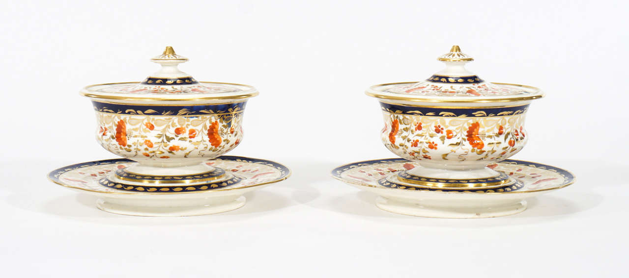 This a pair of unusually shaped sauce tureens with matching under plates. Made by Davenport, circa 1850s, they are round rather than oval or elongated with fitted lids, notched with an opening for a ladle or spoon. Subtly decorated in an Imari