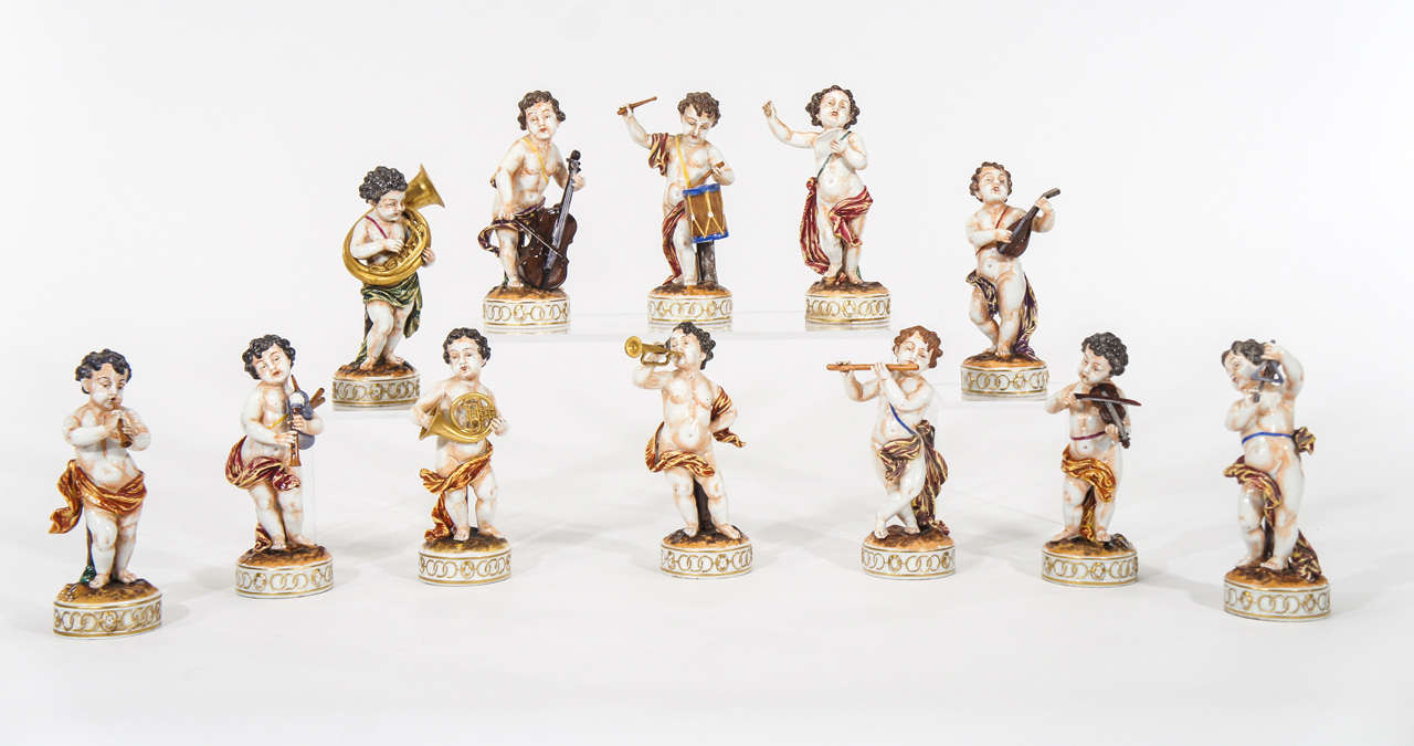 Set of 12 hand-painted porcelain putti figurines depicting musicians each playing a different instrument including the conductor, flautist, triangle player, drummer, cellist, etc. Each figure is beautifully molded and detailed with hand-painted