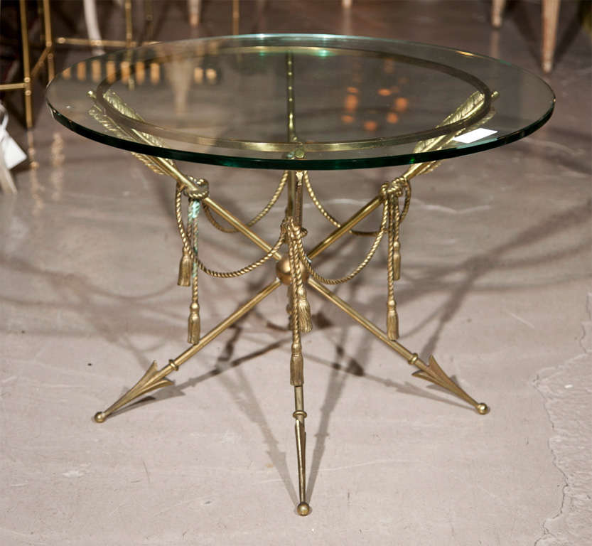 A quad based arrow and tassel form end table. The heavy bronze base table having a centre ball holding a group of four feathered arrows decorated with hanging tassels. The clear glass top to be replaced with a gilt gold top which is in shipping.