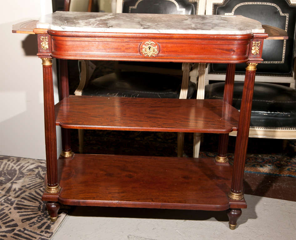 A Mahogany three tier dessert stand / server. Maison Jansen marble top sitting on a lower drawer flanked by side pull out serving trays. The bottom shelves surrounded by flutted columns starting and ending in bronze caps.