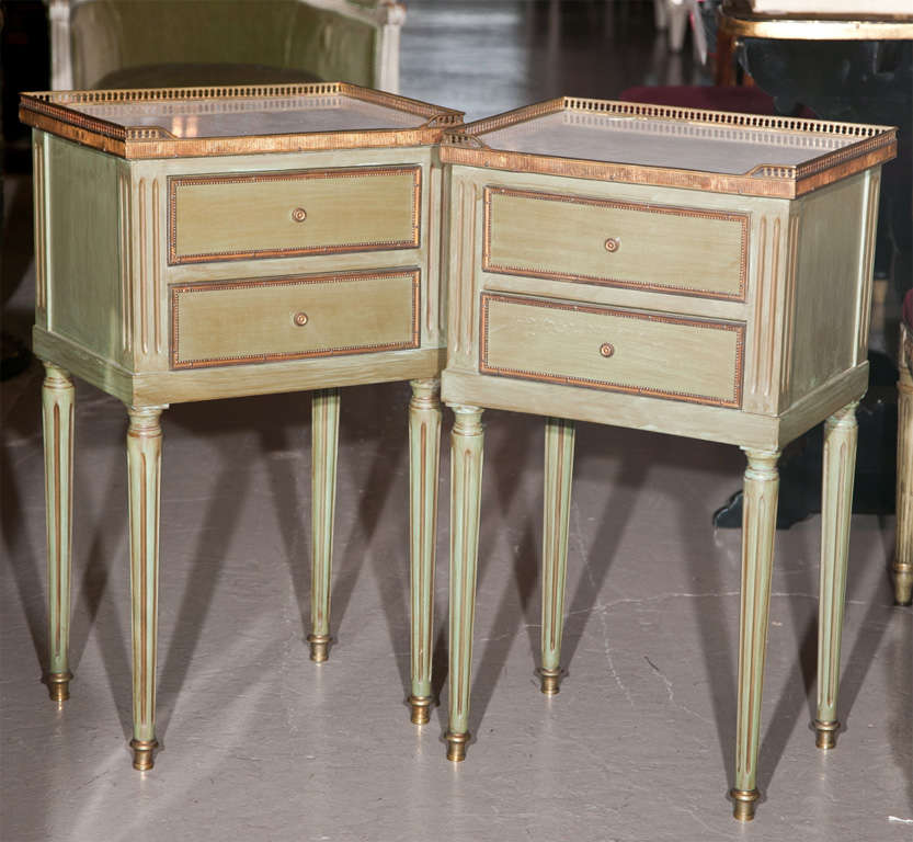 Pair of French stands or end tables, circa 1960s, overall green distress-painted and parcel-gilt, white marble with brass gallery atop a small conforming case fitted with two drawers, raised on fluted tapering legs ending in toupie feet. By Maison