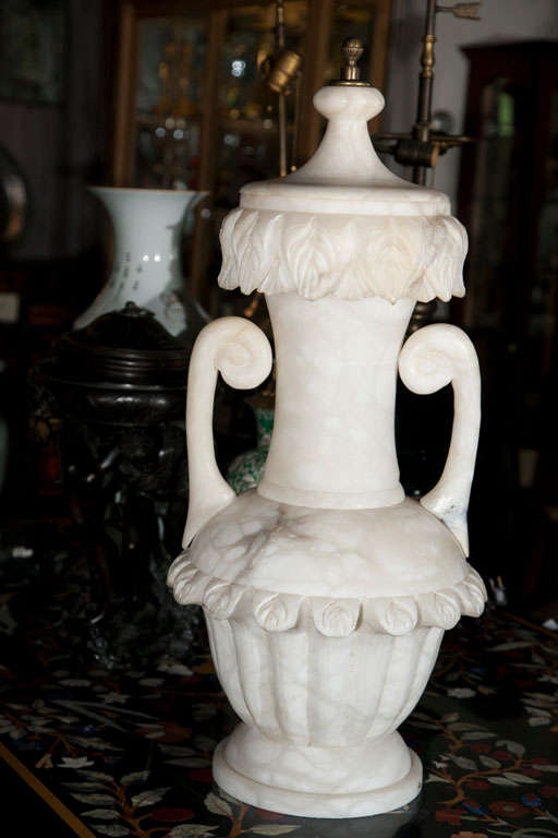 A  2 HANDLE HAND CARVED  ALABASTER URN  WITH A REMOVABLE LID SECURED BY A BRASS FINIAL. INSIDE ARE  BULB SOCKETS FOR CREATING  LIGHT  GLOWING FROM WITHIN. THE HANDLES SEPARATE FROM THE BODY AND PINNED ON