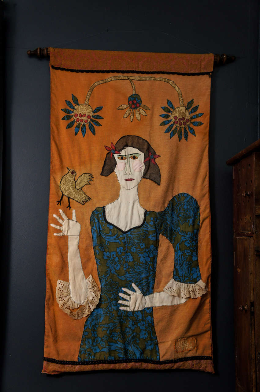 Here is an amusing folk art tapestry of a girl and a bird with flowers. The tapestry is made of found fabric that comprise the dress and sleeves and the bird and flowers.