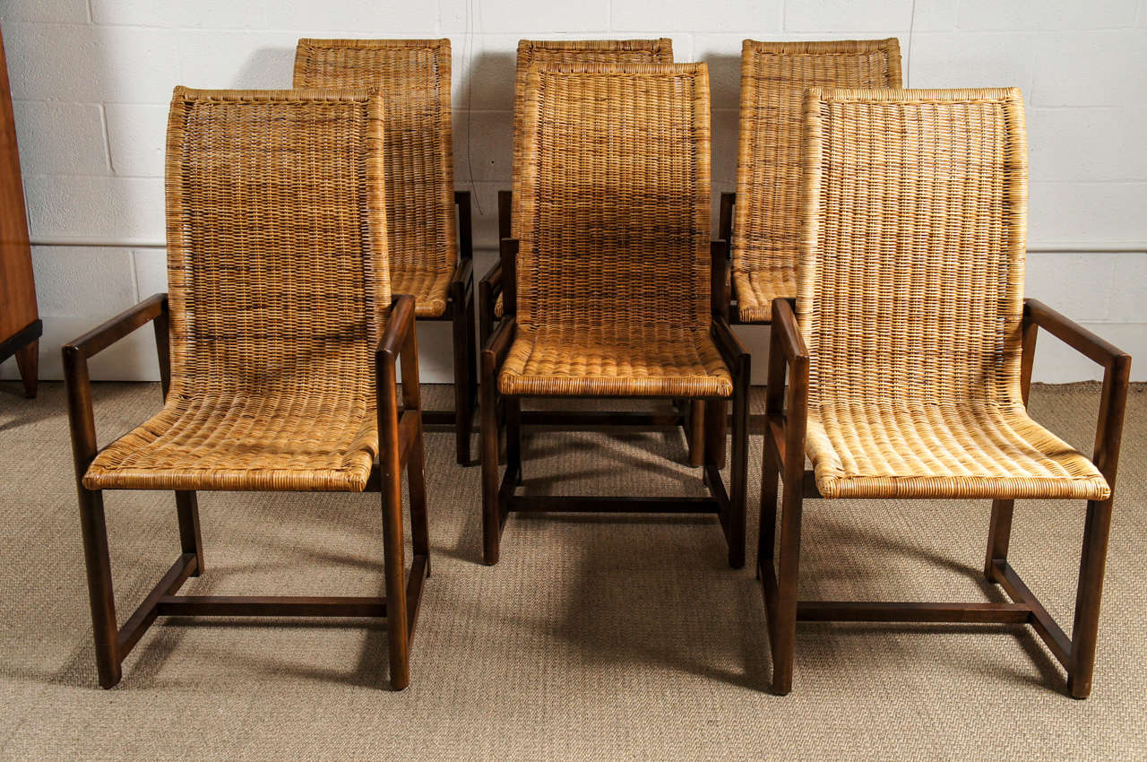 Here is a set of six rattan dining chairs with a curved back and walnut stained wood frames. There are two arm chairs in this set.