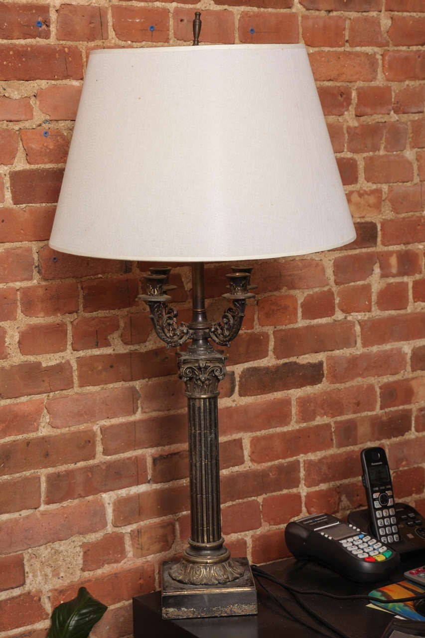 This elite table lamp is a beautiful antique piece with four candelabra and one lighting with a cup and one bulb. Its iron detailed body and Corinthian base creates a sophisticated lighting piece. The top of the linen shade measures 12.25