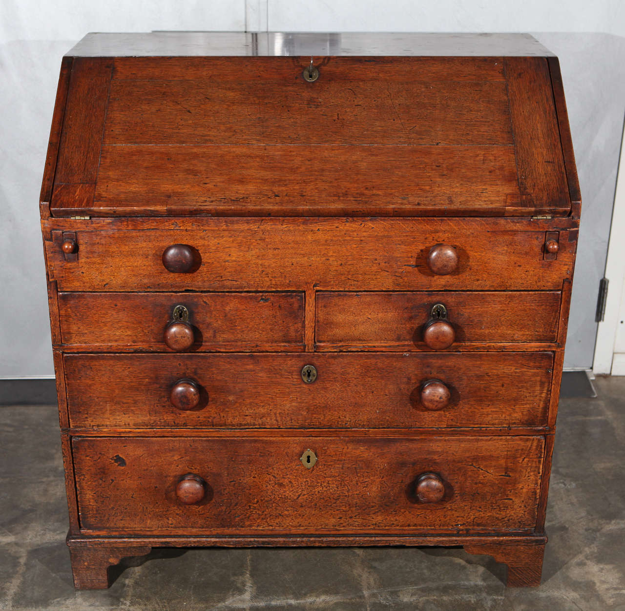 This is a wonderful small-scale oak bureau on bracket feet. This handsome bureau opens to reveal a sweet little desk. The desk holds five small drawers and a center well that leads to two secret compartments at the back of the two side drawers. In