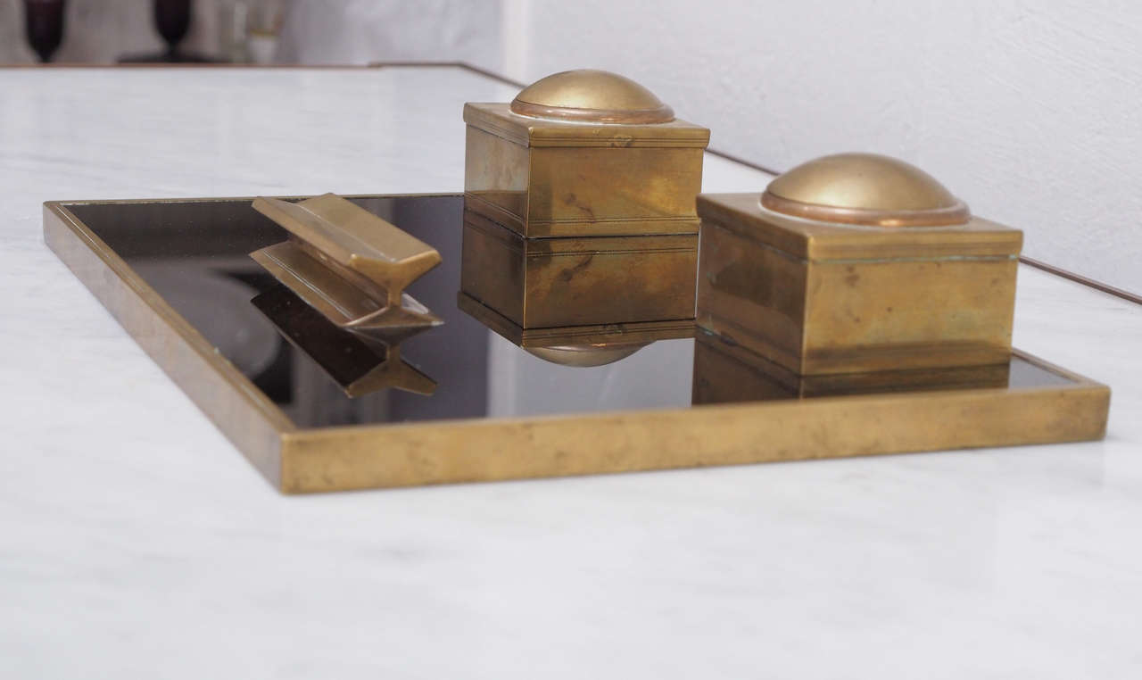 French circa 1940 black glass and brass desk set. The base of this desk set is a rectangle of thick black glass rimmed by brass. Two square brass boxes each house a glass pot for ink. The lid of each box has a dome.