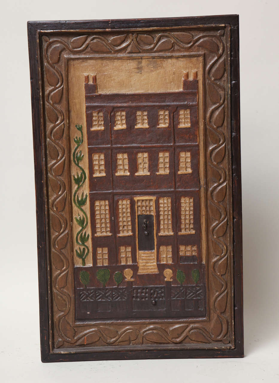 Charming and quirky carved and painted panel depicting a Georgian house, with trailing vine to one side, a lattice work fence with topiary shrubs and surrounded by a trailing vine border, in original polychrome paint.

Ex collection Andras Kalman.