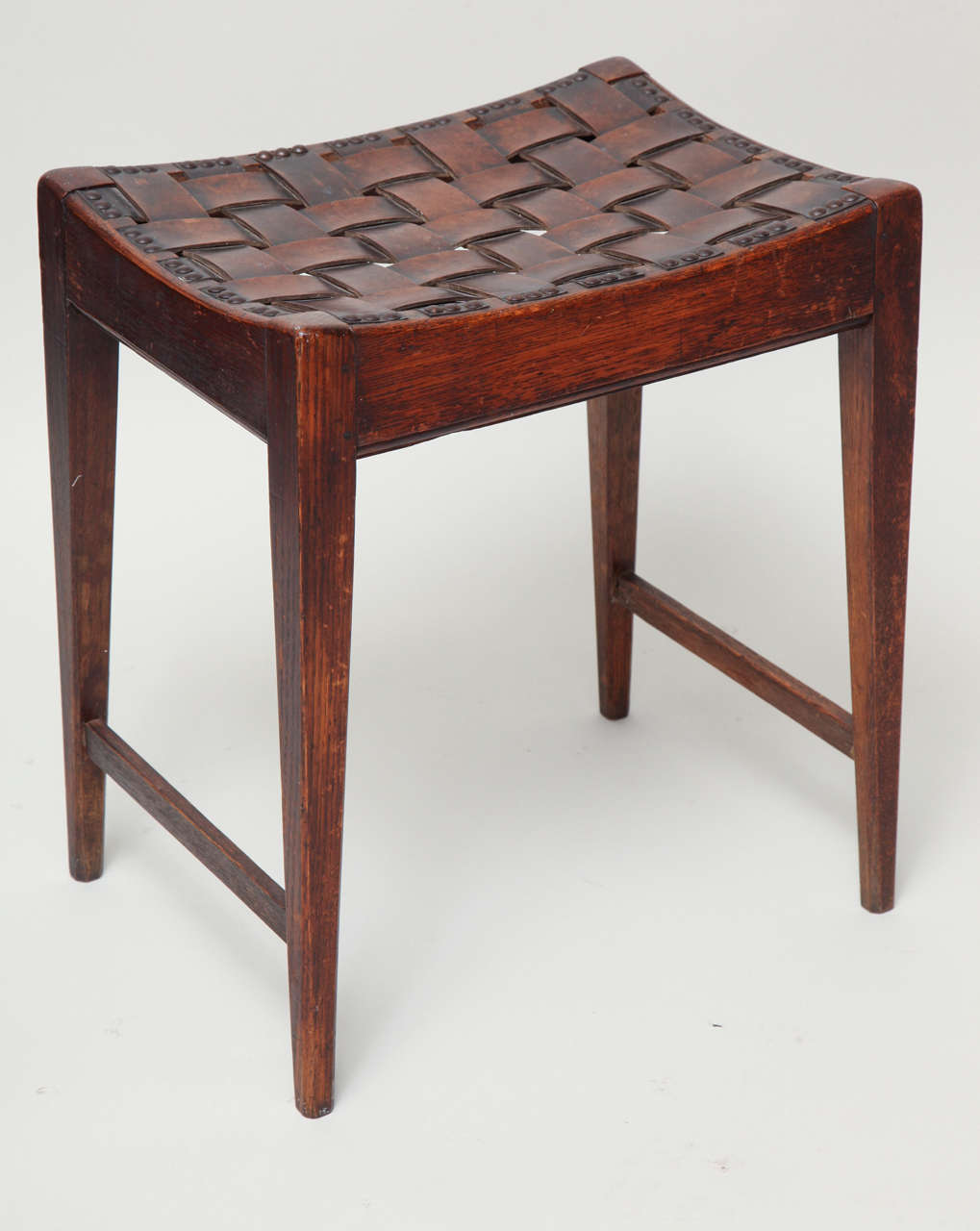 Very good English Arts and Crafts stool made by Arthur Simpson of Kendall, the original leather woven strap work seat on concave rails, the frame in nicely patinated oak, with square tapered legs joined by bar stretchers.