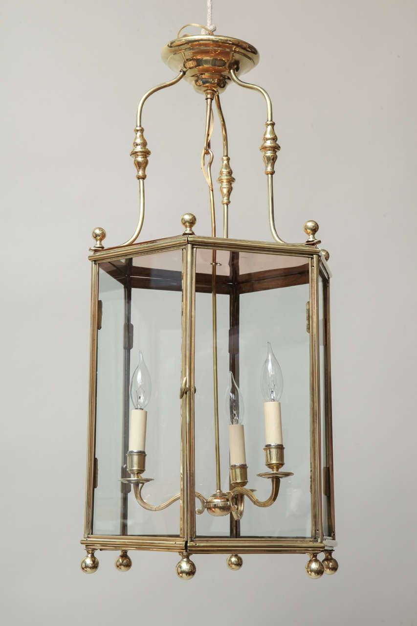 Fine early 20th Century brass hexagonal hall lantern, the three shaped supports held by ball finials, the molded sides encasing original three armed fixture, the base with ball finials, the whole with classic design and pleasing proportions.