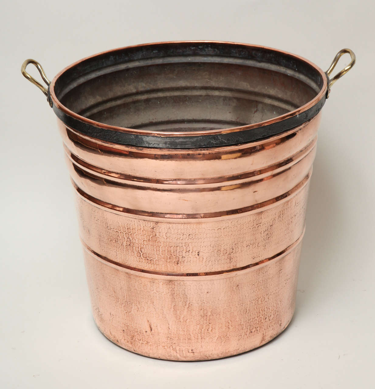 Good 19th century copper bucket having iron band and brass carrying handles, the sides with ribbing and hand-hammered decoration, the whole with pleasing scale and good design. 

Kindling holder, firewood bucket and planter.