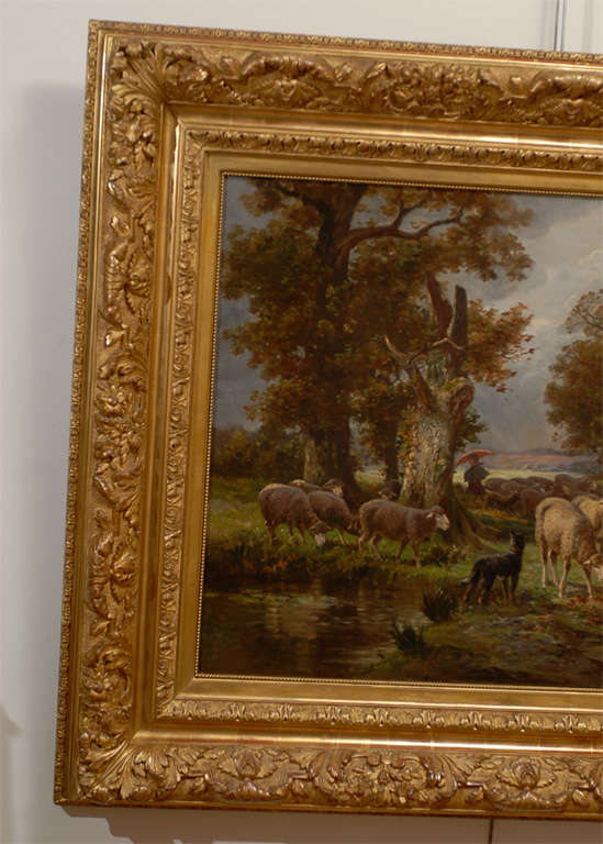 A large oil on canvas painting of sheep in the countryside by French American artist James Desvarreux-Larpenteur from the turn of the century. This painting features a flock of sheep grazing in a forest near a small lake. The sheep are under the