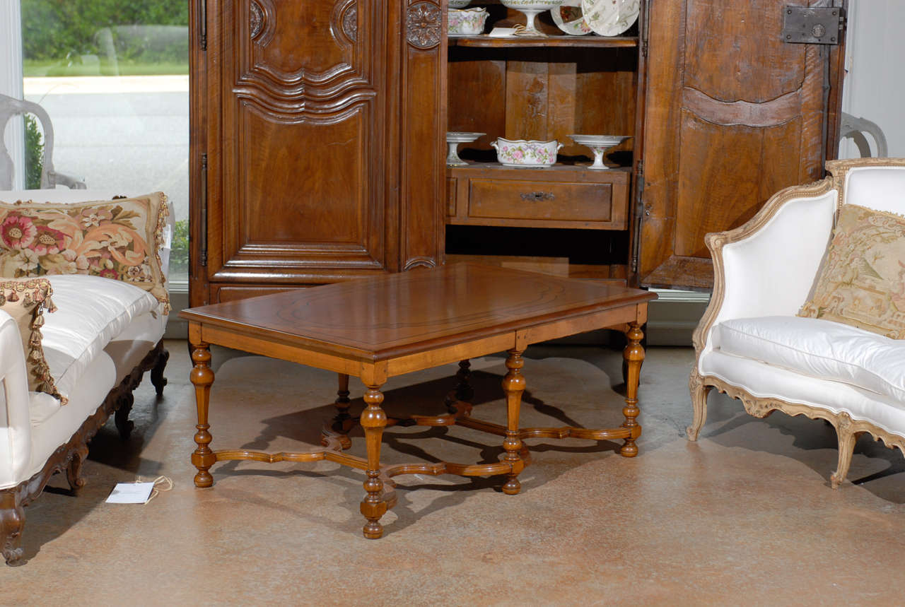 A French Louis XIV style cherry wood coffee table with inlaid top, turned legs and X-form cross stretchers from the late 19th century. This French Louis XIV style table features an exquisite rectangular top with oval-shaped banded inlay of darker