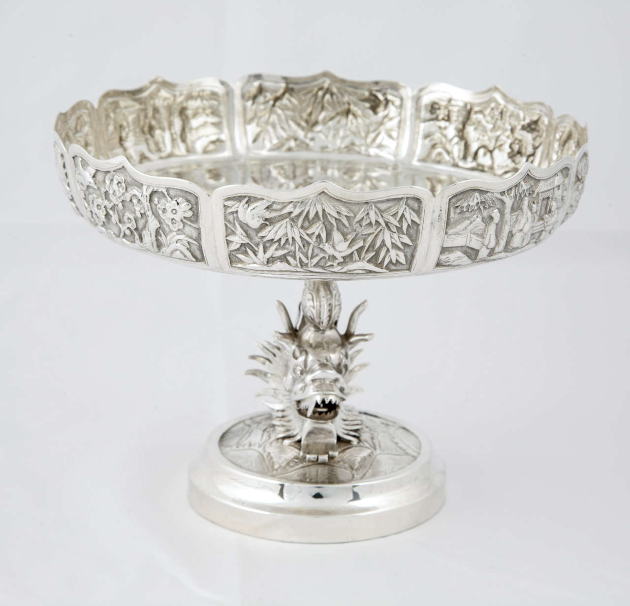 Pair of Chinese export silver tazzas standing on a dragon stem. The panels around the top decorated with a village scene, prunus, dragons and bamboo. The dish, Stand and base are held together by a single rod secured underneath the base. They are